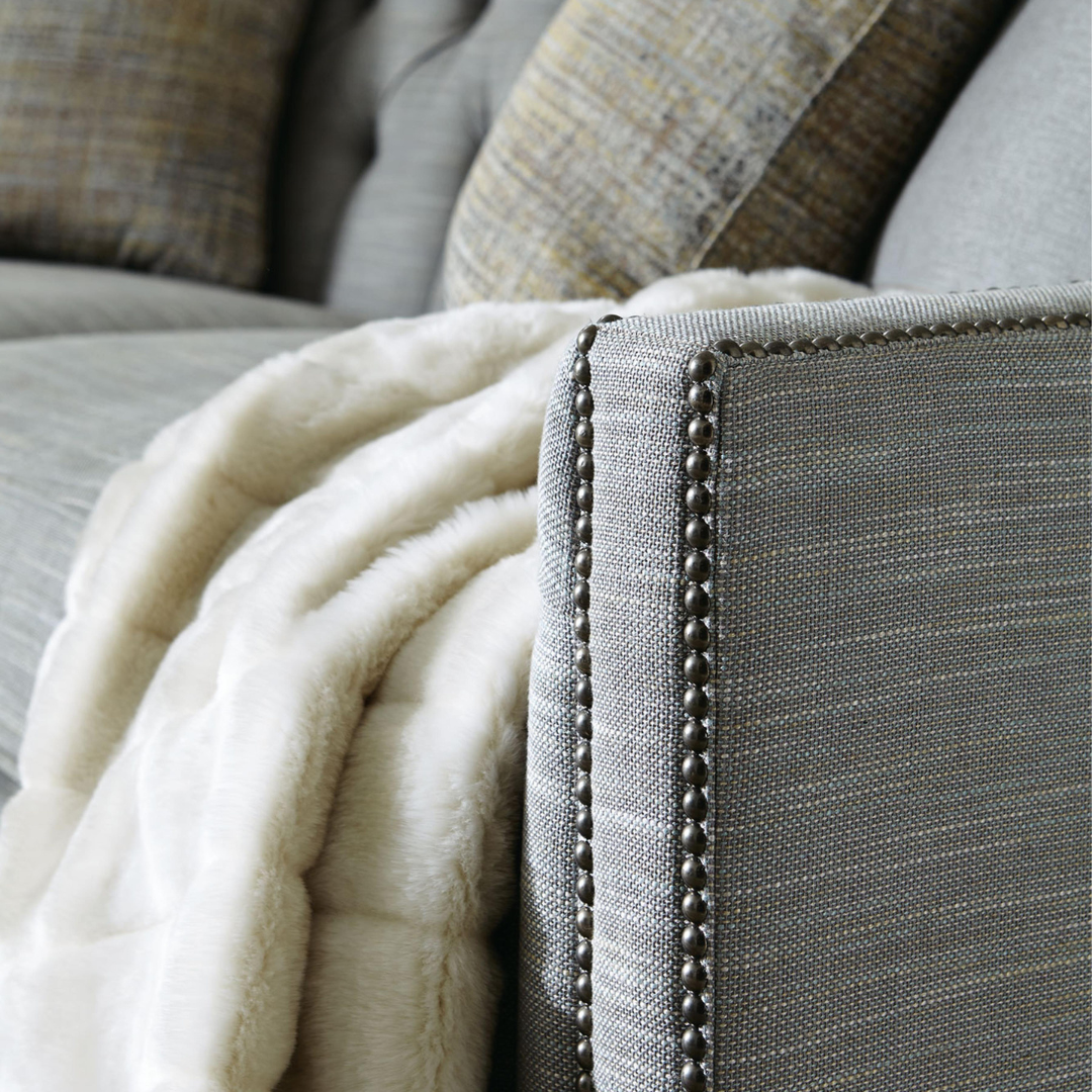 Close-up of Bernhardt Candace 3-Seater Tufted Fabric Sofa arm with nailhead trim detail, shown with a soft cream throw blanket and patterned pillows